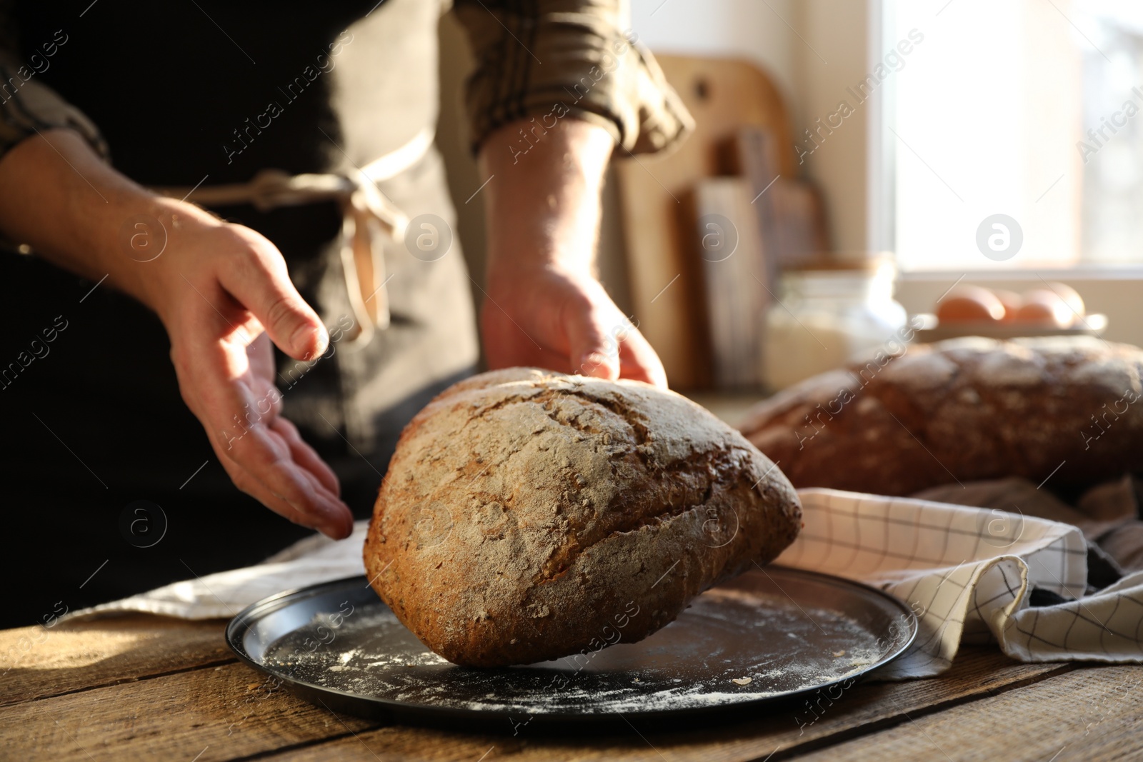 Photo of Man holding loaf of fresh bread at wooden table indoors, closeup