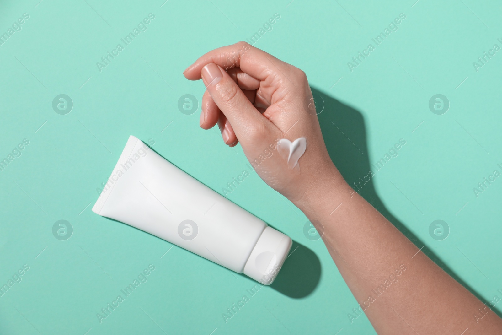 Photo of Woman with tube of hand cream on turquoise background, top view