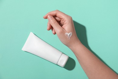 Photo of Woman with tube of hand cream on turquoise background, top view