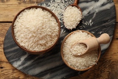 Photo of Raw basmati rice, bowls, spoon and scoop on wooden table, top view