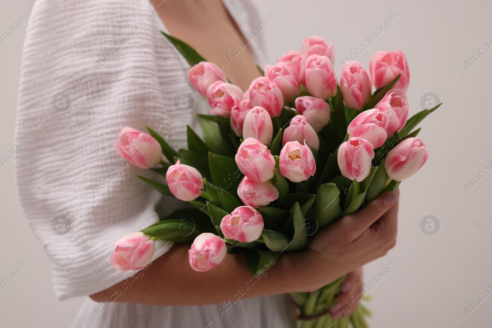 Photo of Woman with bouquet of beautiful fresh tulips on light grey background, closeup