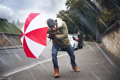 Photo of Man with colorful umbrella caught in gust of wind on street
