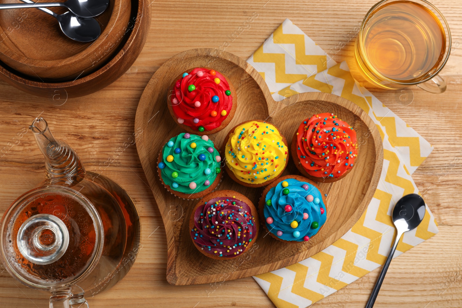 Photo of Delicious cupcakes with colorful cream and sprinkles served on wooden table, flat lay