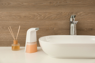 Photo of Modern automatic soap dispenser near sink in bathroom