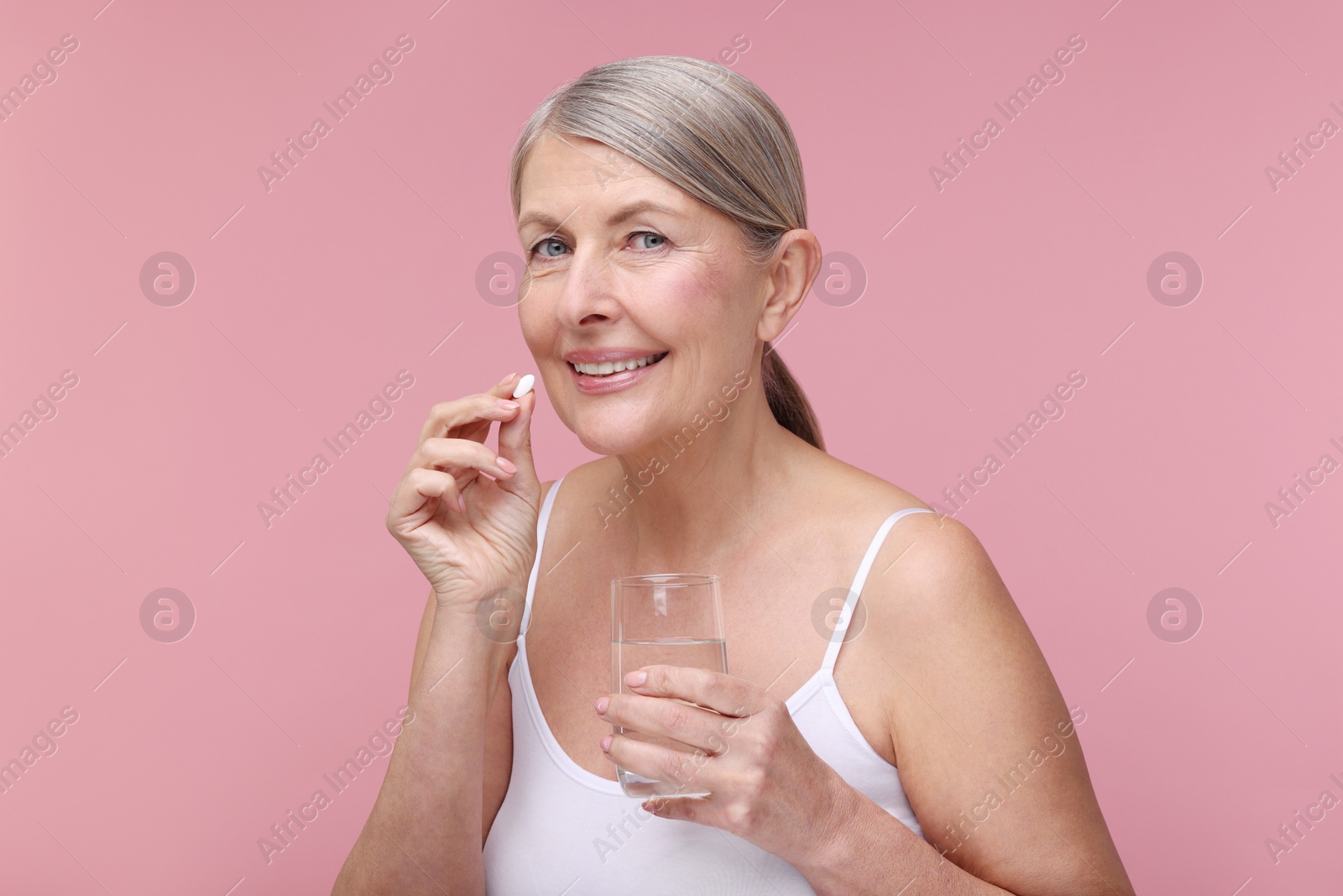 Photo of Beautiful woman with vitamin pill and glass of water on pink background