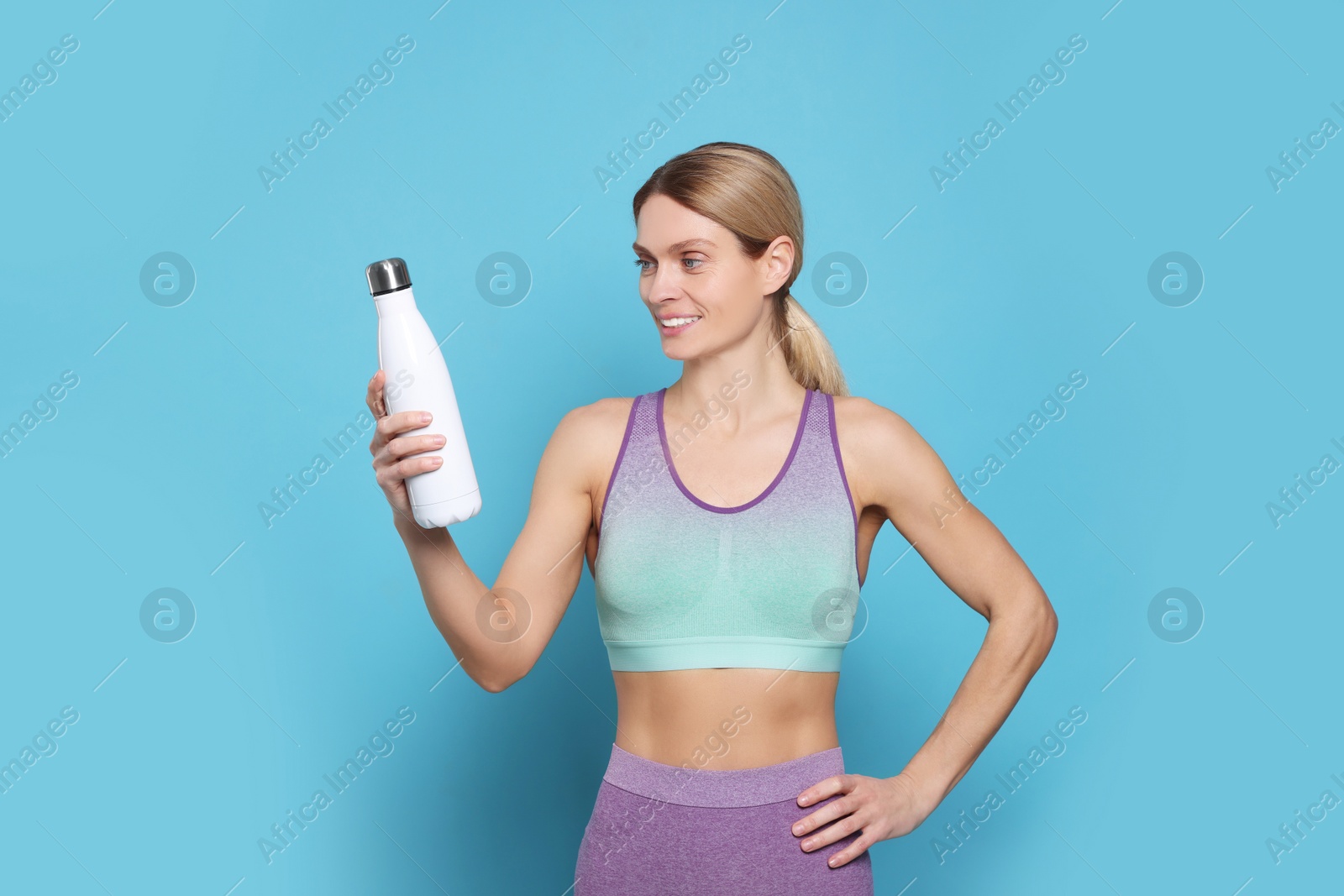 Photo of Sportswoman with thermo bottle on light blue background