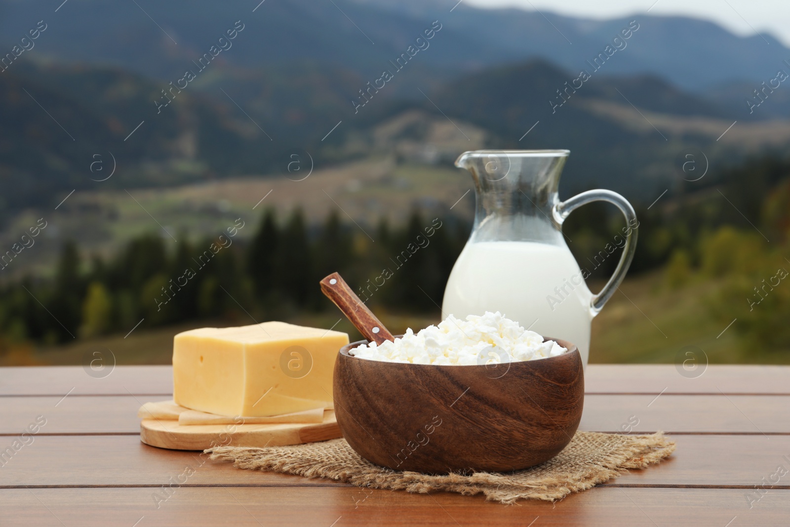 Photo of Tasty cottage cheese and other fresh dairy products on wooden table in mountains