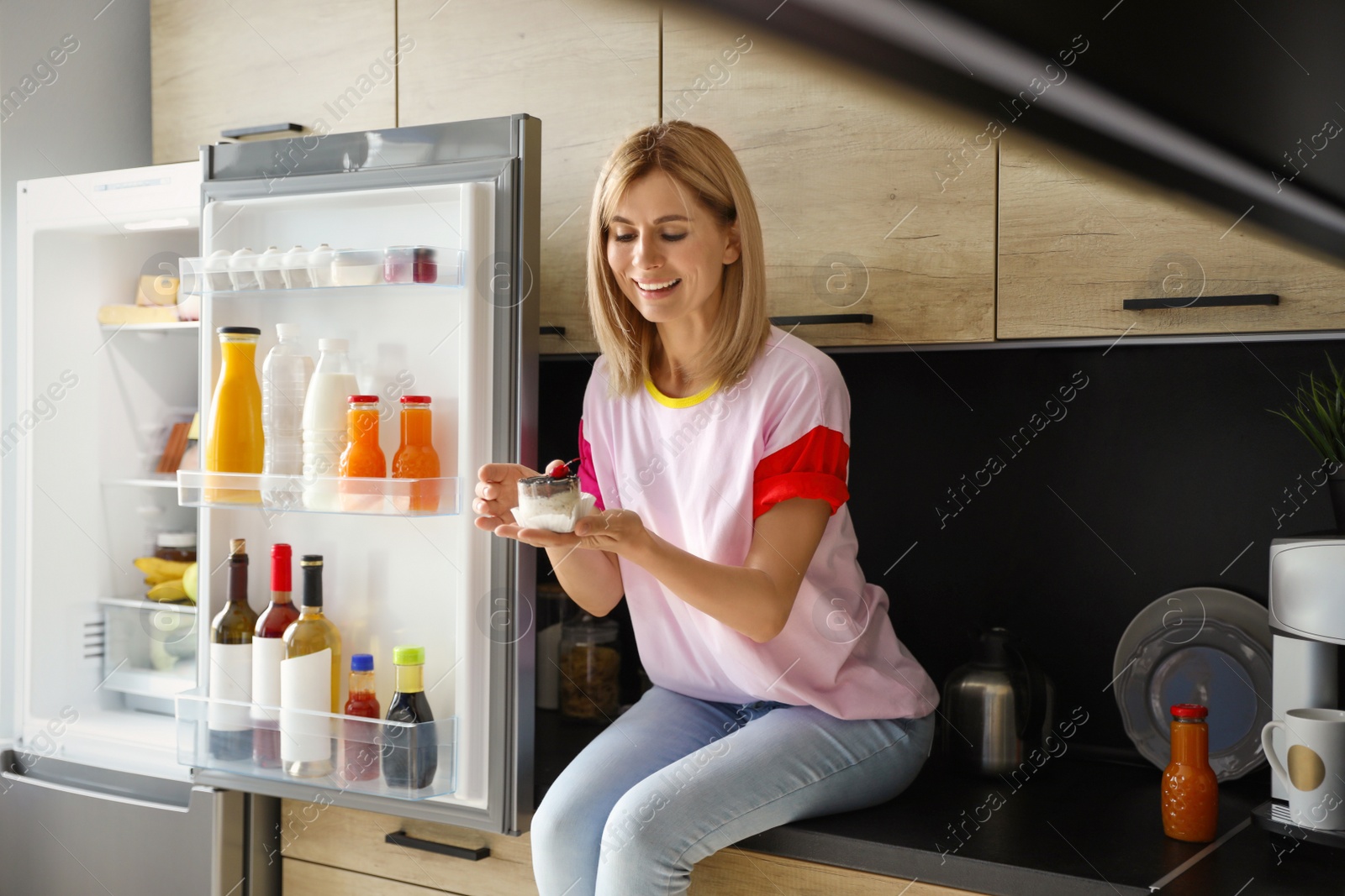 Photo of Woman with dessert near refrigerator in kitchen