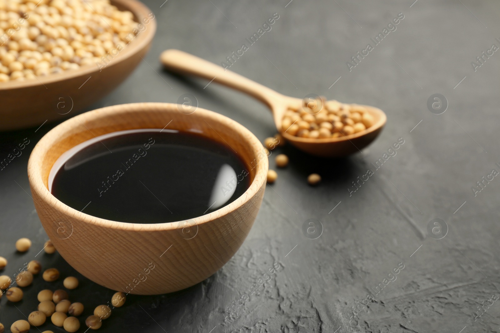 Photo of Tasty soy sauce in bowl and soybeans on black table, closeup. Space for text