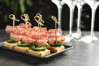 Photo of Tasty canapes with salami, cucumber and cream cheese on grey table. Space for text