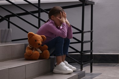 Photo of Child abuse. Upset girl with toy sitting on stairs