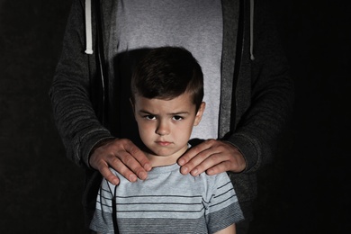 Photo of Scared little boy and adult man on dark background. Child in danger