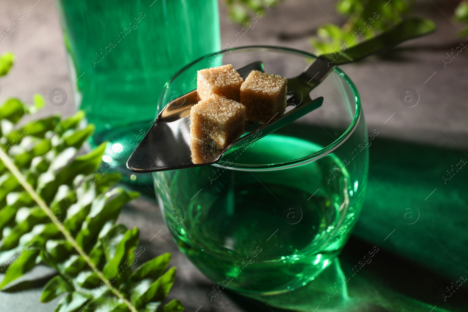 Photo of Absinthe in glass, spoon with brown sugar cubes on table, closeup. Alcoholic drink