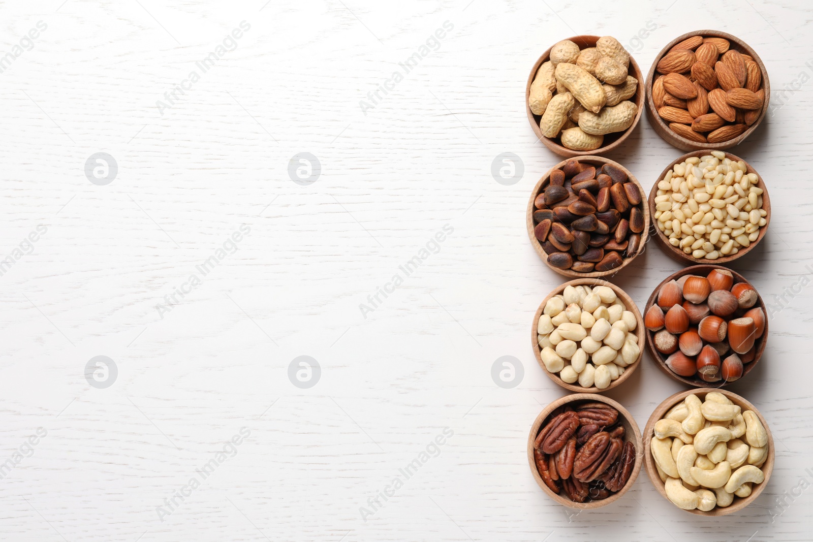 Photo of Bowls with different organic nuts and space for text on white wooden background, top view. Snack mix