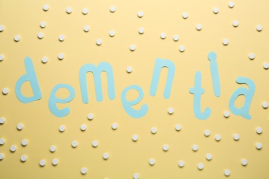 Photo of Word Dementia made of paper letters and pills on beige background, flat lay