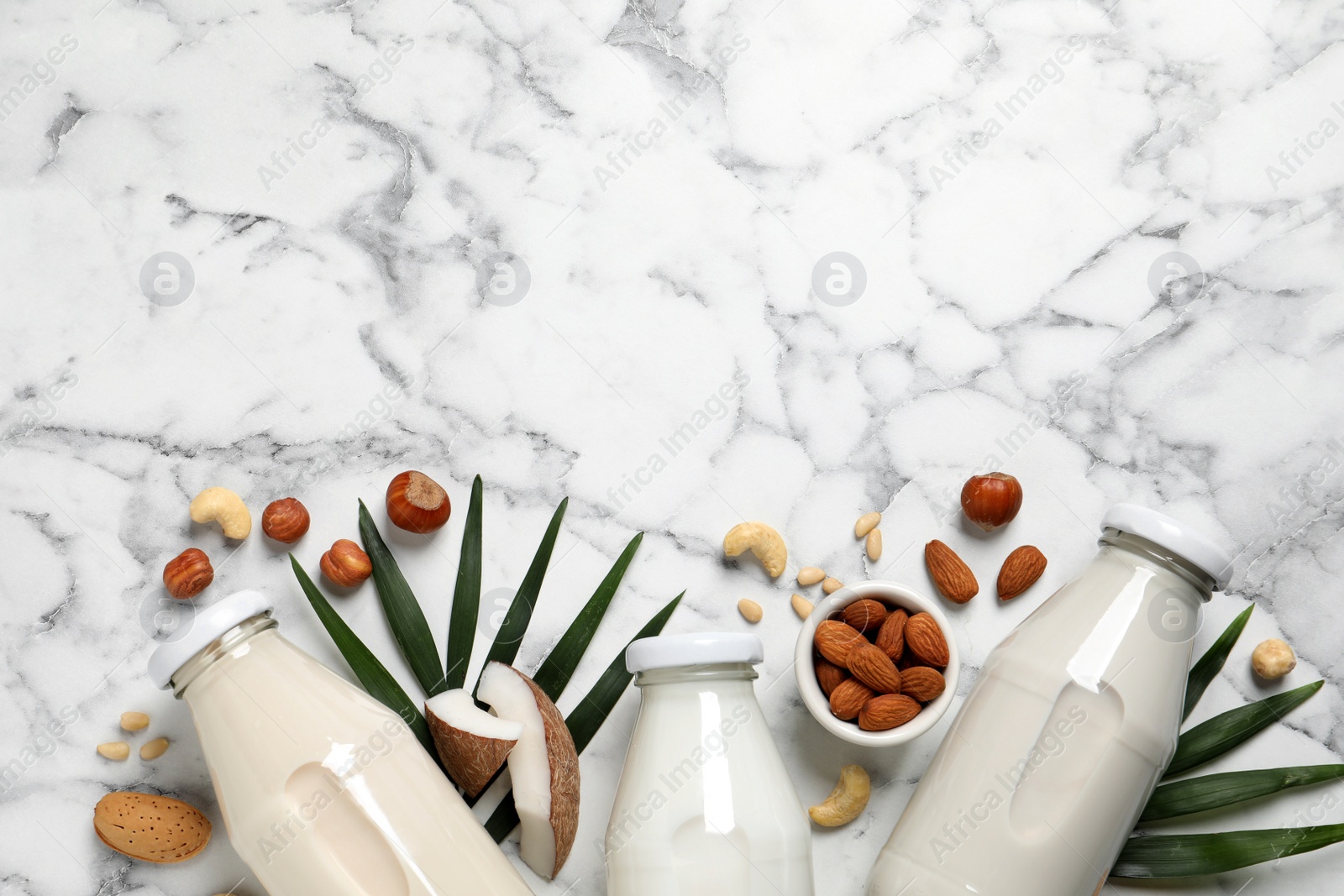 Photo of Vegan milk and different nuts on white marble table, flat lay. Space for text