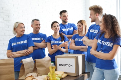 Team of volunteers near table with food donations indoors