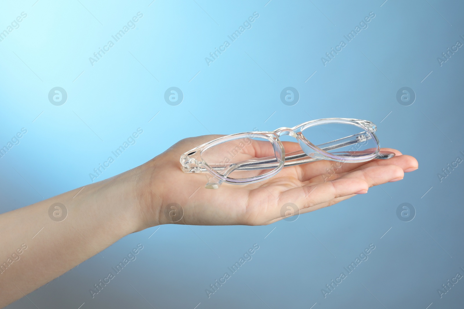 Photo of Woman holding glasses with transparent frame on light blue background, closeup