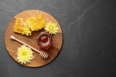 Photo of Sweet honey in jar, dipper, chrysanthemum flowers and pieces of honeycomb on grey textured table, top view. Space for text