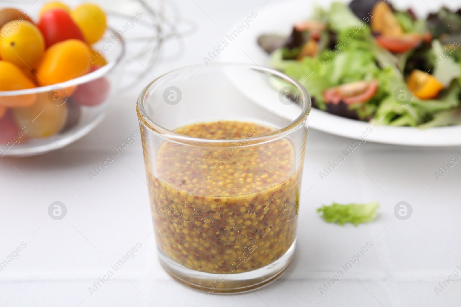 Photo of Tasty vinegar based sauce (Vinaigrette) in glass on light tiled table, closeup