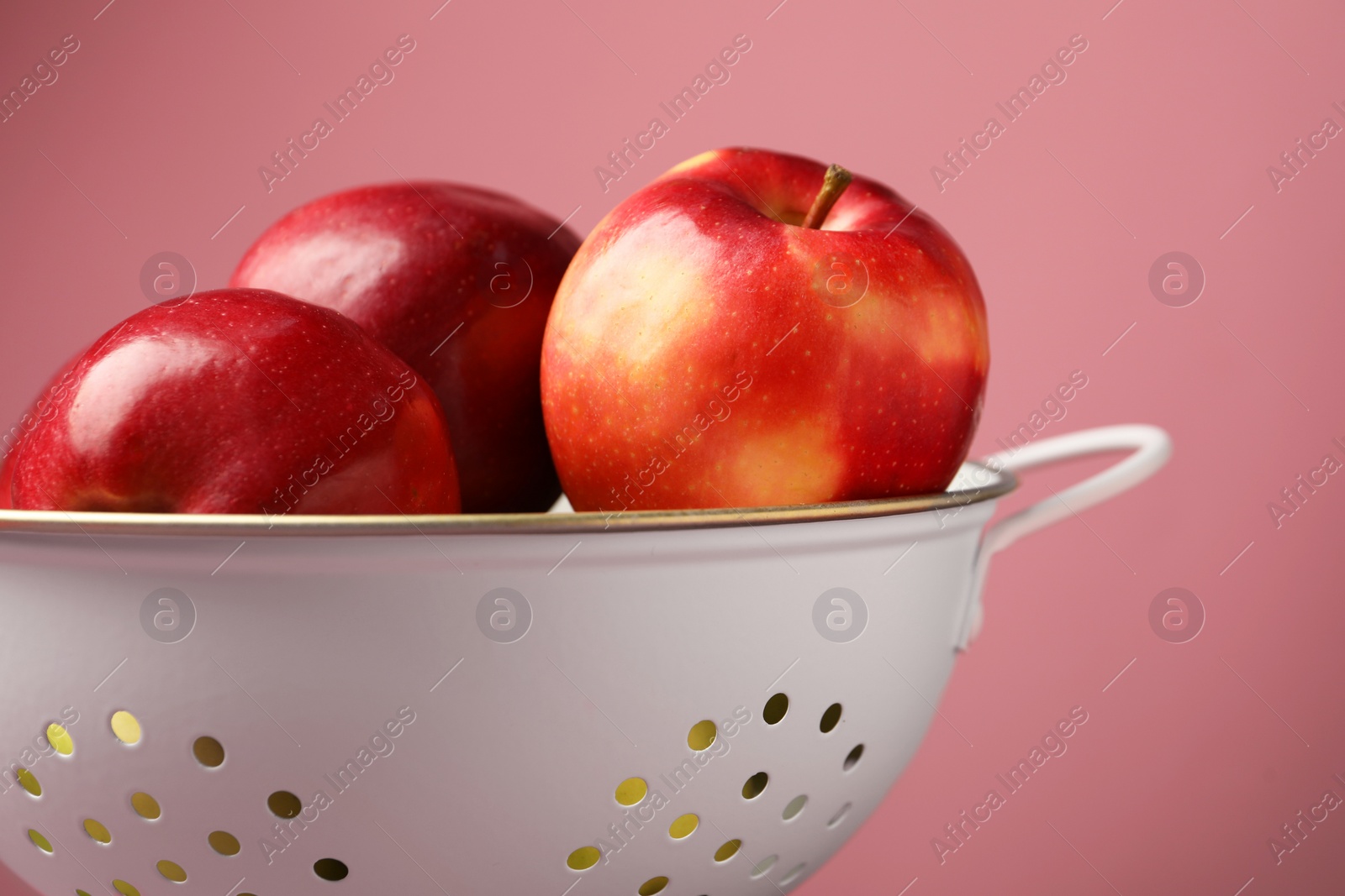 Photo of Colander with fresh apples against pink background, closeup