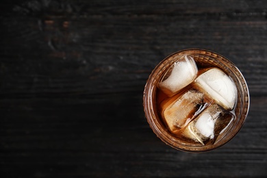 Glass of refreshing cola with ice cubes on wooden background, top view. Space for text
