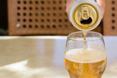 Man pouring beer from can into glass at table, closeup. Space for text