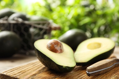 Halves of delicious ripe avocado on wooden board against blurred background