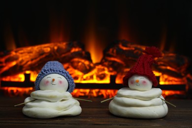 Photo of Cute decorative snowmen in hats on wooden floor near fireplace