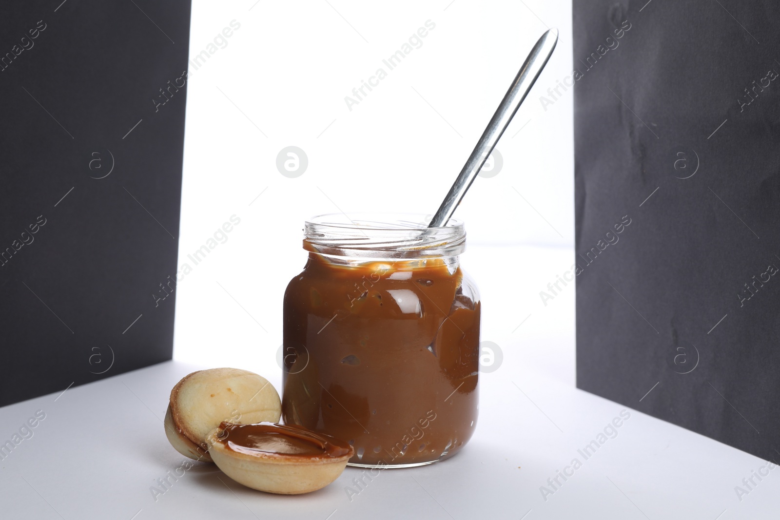 Photo of Jar with boiled condensed milk, spoon and walnut shaped cookies on white background