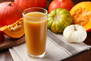 Tasty pumpkin juice in glass and different pumpkins on wooden table