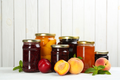 Glass jars with different pickled fruits and jams on white wooden background