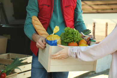 Photo of Courier giving crate with products to client outdoors, closeup. Food delivery service