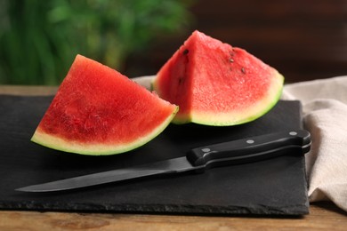 Photo of Pieces of delicious ripe watermelon on slate board indoors, closeup