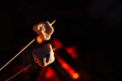 Photo of Delicious marshmallows roasting over bonfire outdoors at night, closeup. Space for text
