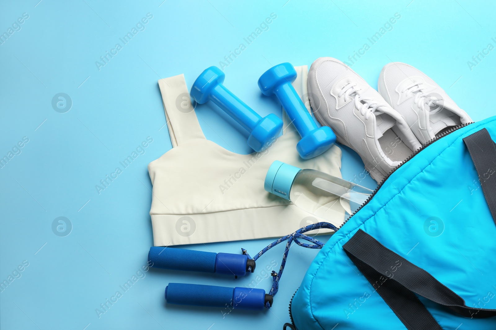 Photo of Composition with gym bag and sports items on light blue background, above view