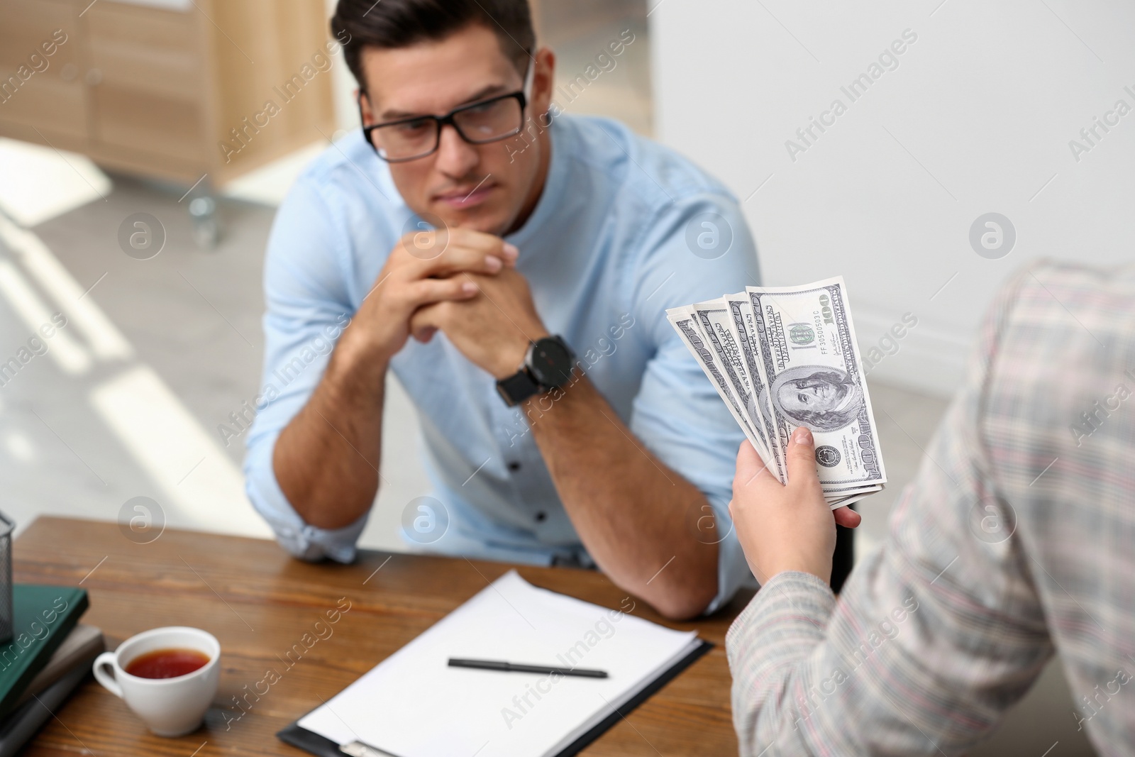 Photo of Woman offering bribe money to man at table