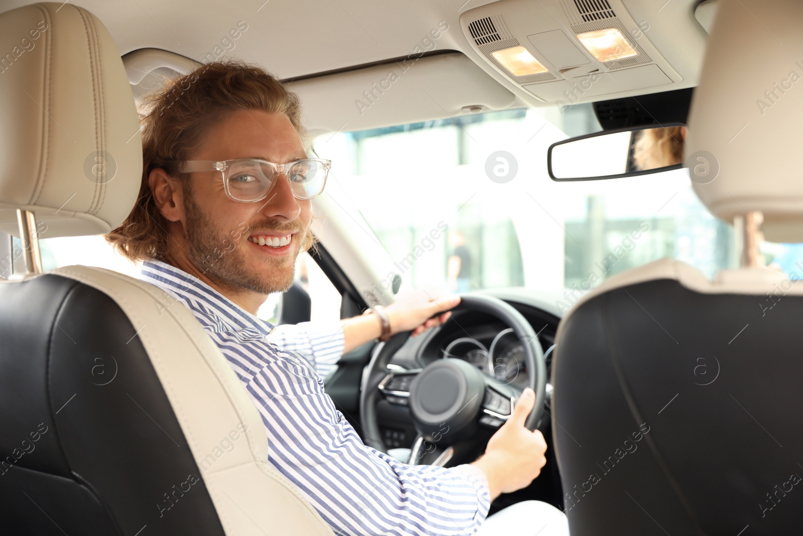 Photo of Attractive young man driving his luxury car, view from backseat