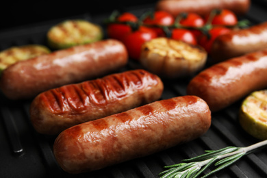 Photo of Cooking delicious fresh sausages with vegetables on modern grill, closeup
