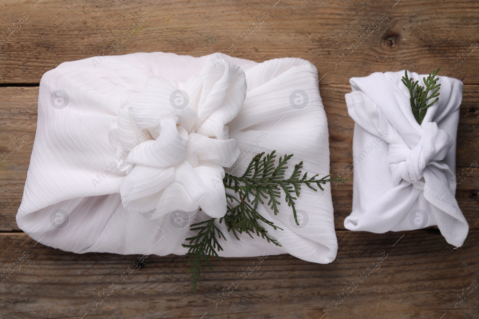 Photo of Furoshiki technique. Gifts packed in white fabric and thuja branches on wooden table, flat lay