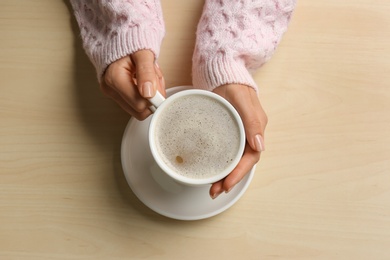 Photo of Woman holding cup of coffee at wooden table, top view