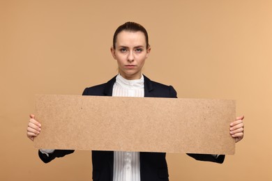 Woman holding blank cardboard banner on beige background, space for text