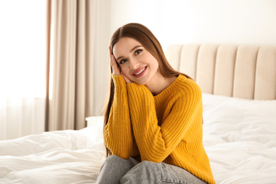 Young woman wearing warm sweater on bed at home. Winter season
