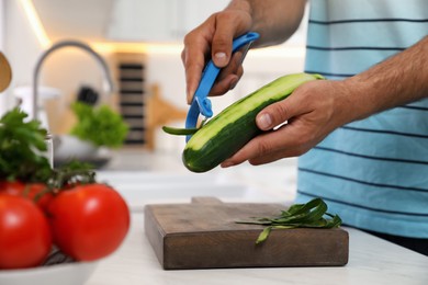 Photo of Man peeling cucumber at kitchen counter, closeup. Preparing vegetable