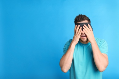 Man with black blindfold on blue background, space for text