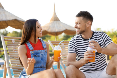 Image of Happy couple with cups of refreshing drink resting in deck chairs 