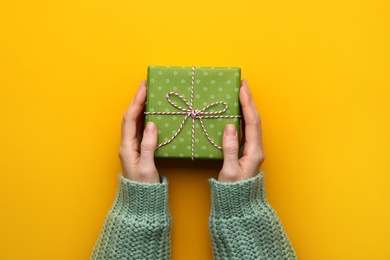 Photo of Woman holding Christmas gift box on orange background, closeup