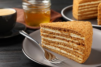 Photo of Slice of delicious layered honey cake served on black wooden table, closeup