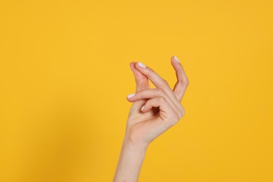 Photo of Woman snapping fingers on yellow background, closeup of hand