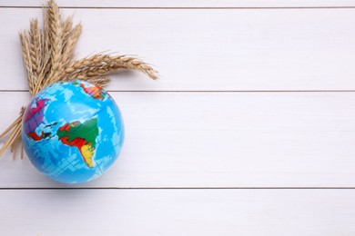 Globe and ears of wheat on white wooden table, flat lay with space for text. Import and export concept